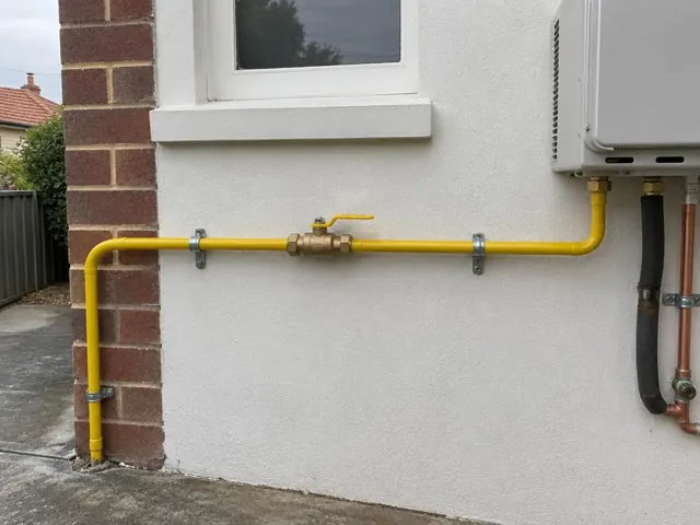 Yellow gas pipe and valve mounted on an exterior brick and rendered wall beside a window in Auburn