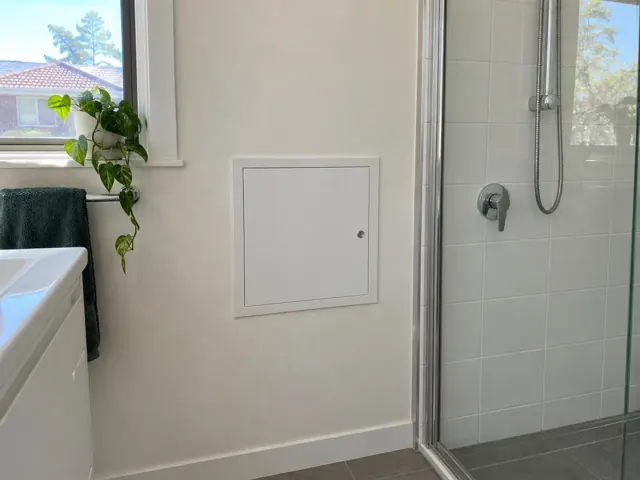 Neat white access panel on a painted bathroom wall beside a tiled shower and window in South Granville